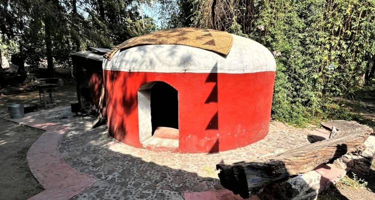 Runde rot-weiße Adobe-Schwitzhüttenstruktur zwischen Bäumen