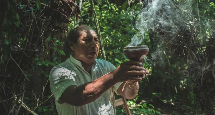 Indigener Schamane führt ein rauchiges Räucherwerk-Ritual in einer üppig grünen Dschungelumgebung durch