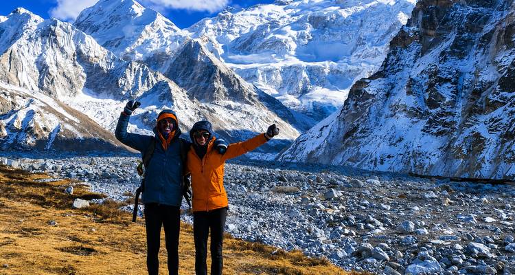 Twee juichende trekkers in felgekleurde jassen vieren feest tussen ruige met sneeuw bedekte Himalaya-bergen.