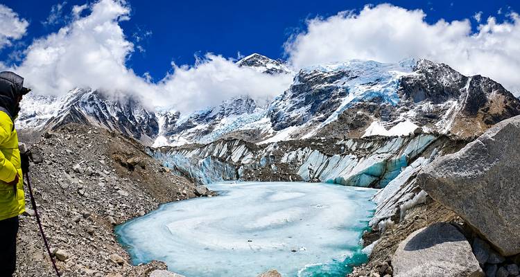 Trekker staart over een turkooise bevroren gletsjermeer omlijst door steile, besneeuwde Himalaya-toppen.
