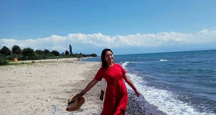 Mujer joven en un vestido rojo vaporoso pasea por la orilla arenosa de un vasto lago alpino.