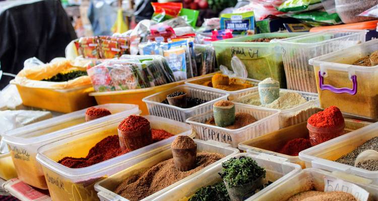 Kleurrijke hoopjes kruiden en specerijen gerangschikt in open marktkuipen met handgeschreven labels.