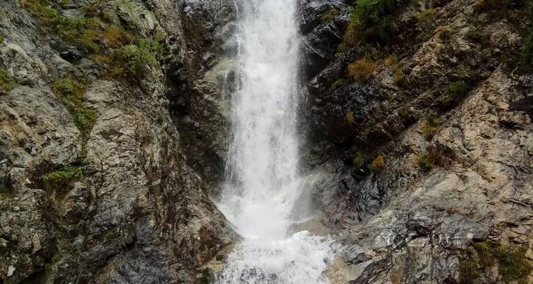Una cascada poderosa se precipita por paredes rocosas escarpadas hacia una poza turbulenta entre acantilados cubiertos de musgo exuberante.