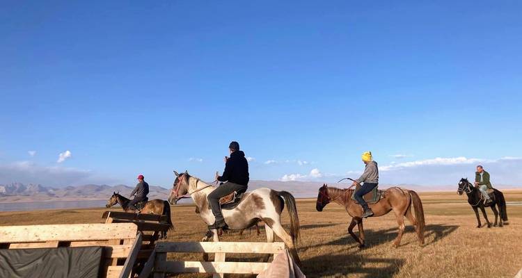 Gruppe von Reisenden, die auf Pferden durch eine weite offene kirgisische Steppe unter einem klaren blauen Himmel reiten.