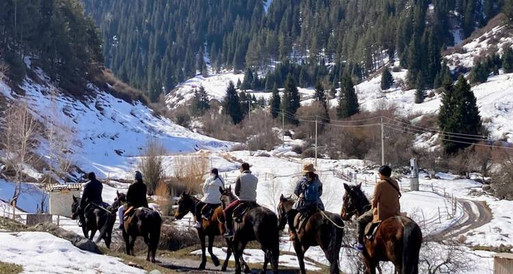 Reiter zu Pferd reisen entlang eines verschneiten Bergpfades, der von immergrünen Wäldern in Kirgisistan gesäumt wird.