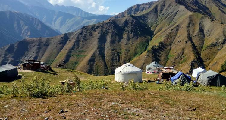 Ansammlung traditioneller Jurten auf einem grasigen Alpenplateau, umgeben von Gipfeln.