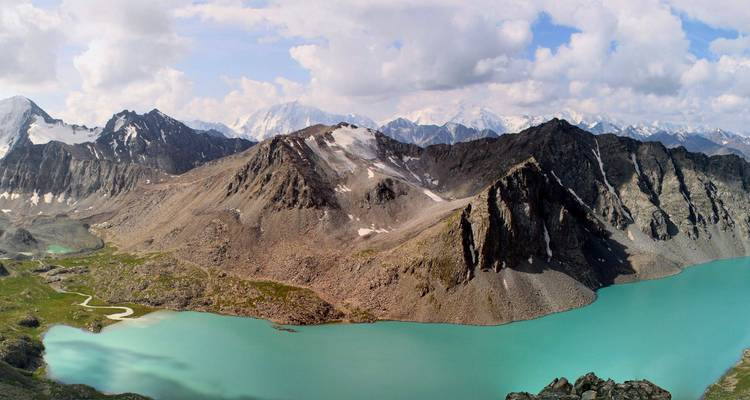 Amplio panorama del lago alpino turquesa y los picos dramáticos de la cordillera Tian Shan de Kirguistán.
