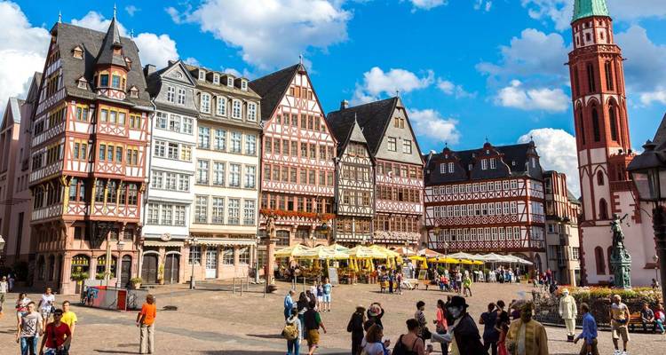 Bunte Fachwerkhäuser umgeben einen lebendigen historischen Platz an einem sonnigen Tag.