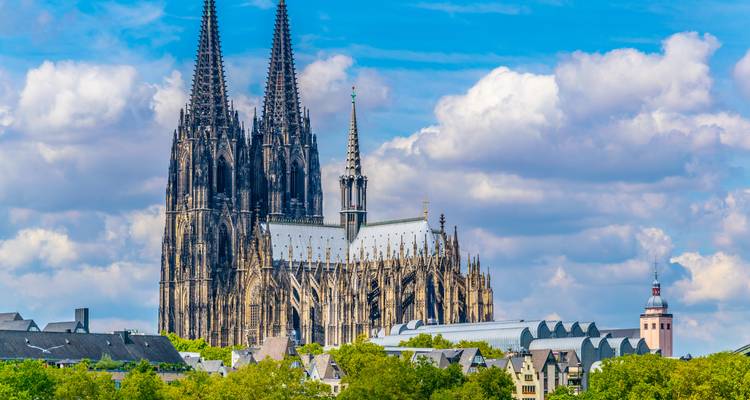 Der ikonische Kölner Dom ragt über die Dächer der Stadt vor einem Hintergrund aus flauschigen Wolken empor.