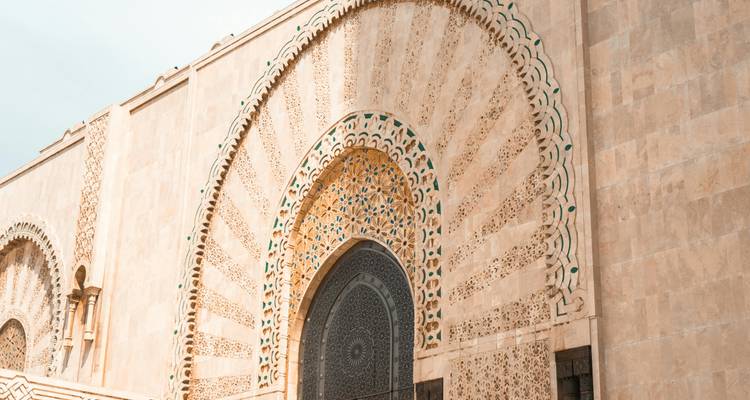 Gedetailleerde gewelfde gevel van de Hassan II-moskee met indrukwekkend steenwerk en groene inlegwerk