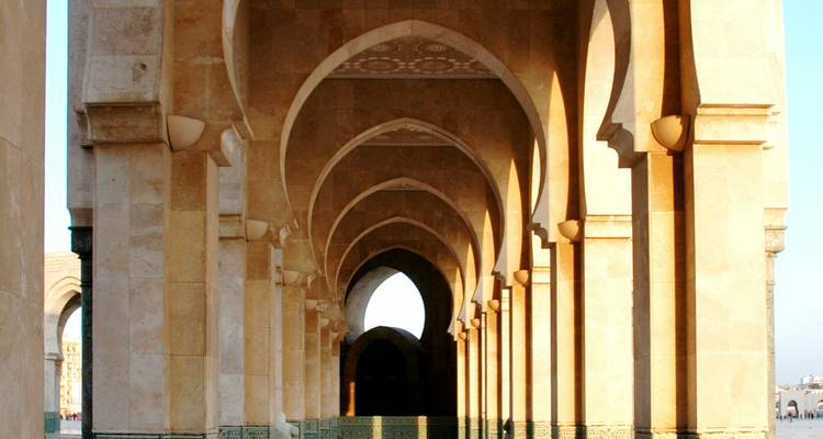 Zonnig binnenplein van de Hassan II-moskee met zich herhalende bogen en gemusterde tegels