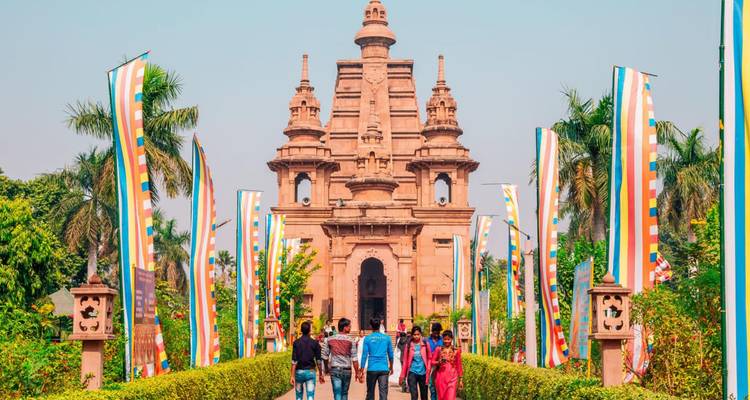 Visitors walking toward a sandstone temple flanked by colorful prayer flags in Sarnath
