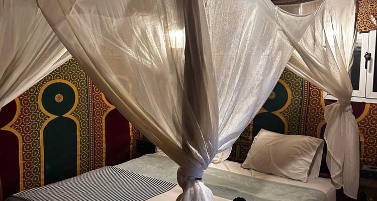 Traditionelles Wüstencamp-Schlafzimmer mit fließenden weißen Baldachinvorhängen und gemusterten Wänden.