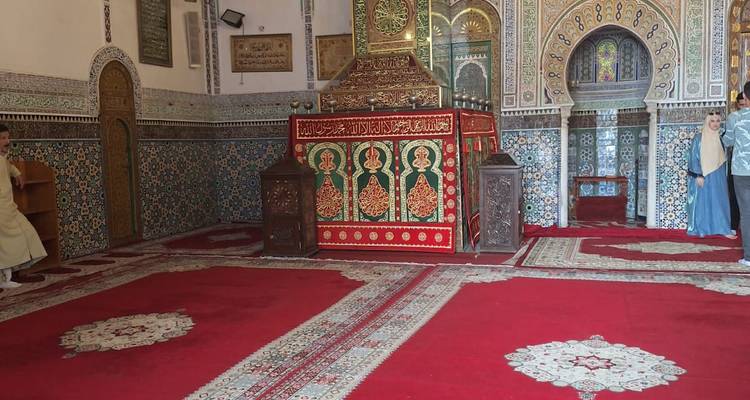 Reichhaltig gefliestes Inneres einer marokkanischen Moschee mit roten Teppichen und kunstvollen Kalligrafie-Tafeln.
