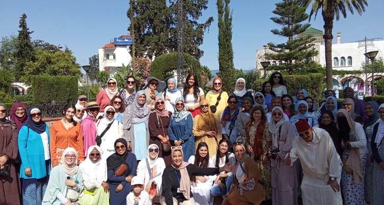 Große von Frauen geleitete Reisegruppe, die in einem Garten mit Palmen und weißer Architektur im Hintergrund posiert.