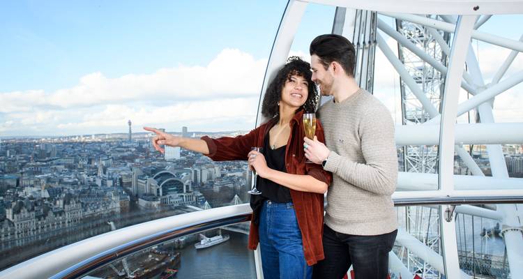 Ein lächelndes Paar mit Champagner bewundert den Panoramablick auf London in einer Glaskapsel des London Eye.