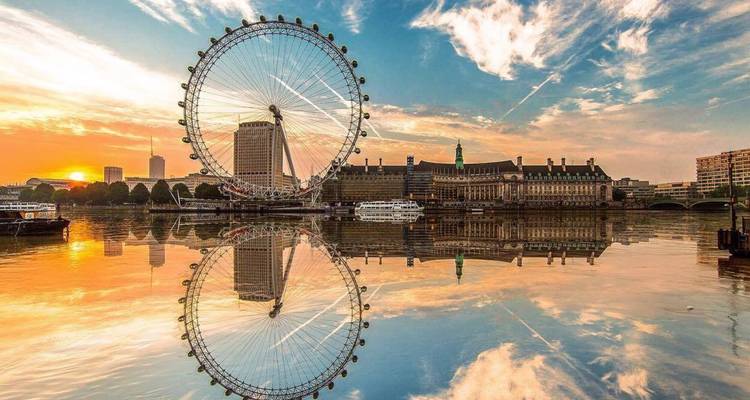 Das London Eye spiegelt sich perfekt in der ruhigen Themse bei Sonnenaufgang mit bunten Wolken darüber wider.