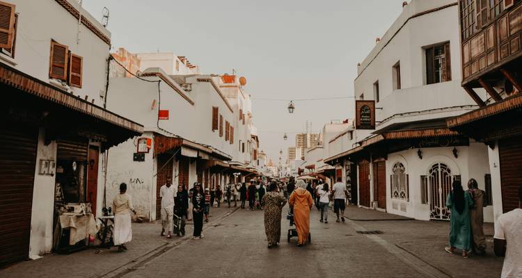 Voetgangersstraat in een Marokkaanse medina met locals en winkelende bezoekers tussen witgekalkte gebouwen bij het invallen van de avond