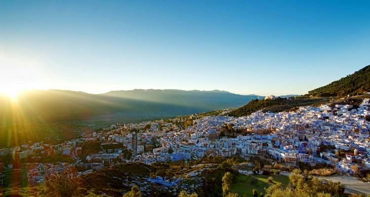 Panoramisch uitzicht bij zonsopgang over het blauw geschilderde heuveldorp Chefchaouen met bergen eromheen.