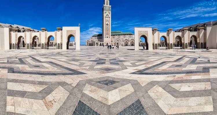 Vasta plaza de mármol con patrones geométricos que conduce a la Mezquita Hassan II bajo un cielo azul vivido