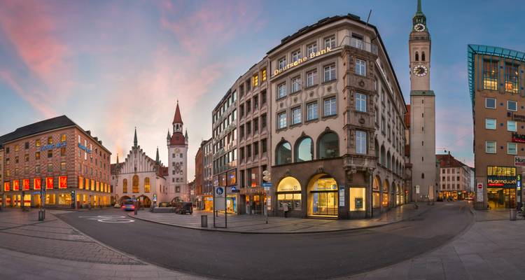 Panoramablick auf Münchens historisches Zentrum bei Morgendämmerung mit pastellfarbenem Himmel und beleuchteten Uhrtürmen entlang der Straßen.