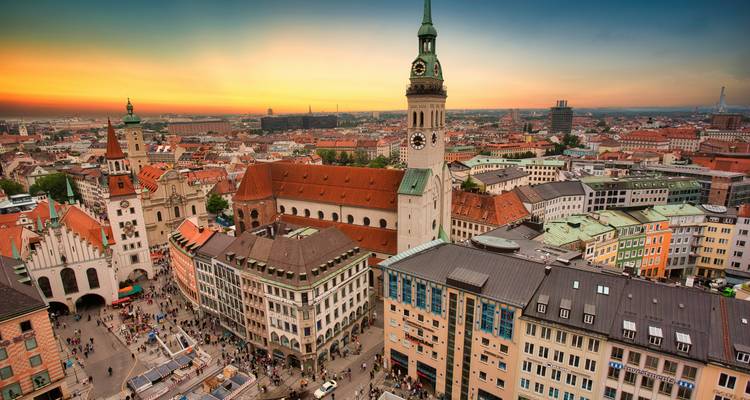 Sonnenuntergangsblick über Münchens Skyline mit historischen Kirchen, Türmen und Dächern, die unter einem farbenfrohen Himmel leuchten.