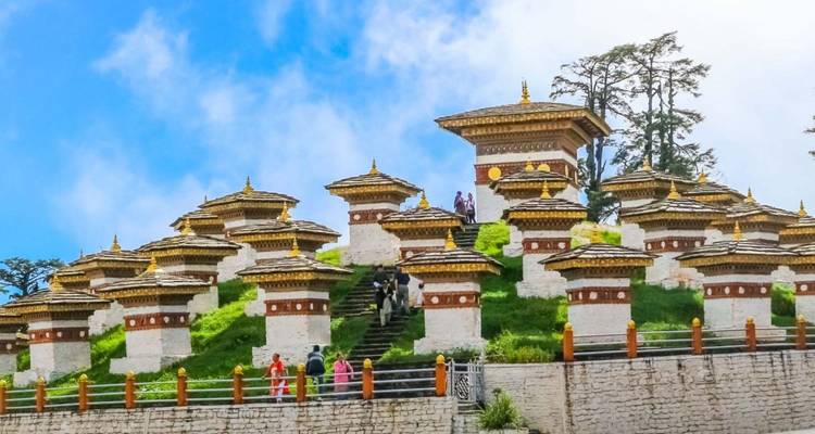 Filas de chortens blancos y dorados ubicados en una colina cubierta de hierba bajo un cielo azul brillante.