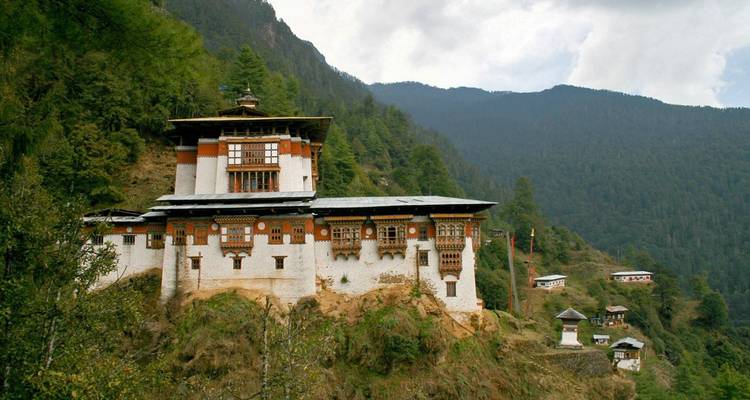 Monasterio bhutanés tradicional encaramado en una ladera boscosa con un telón de fondo de montañas.