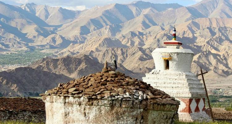 Alte Stupas aus Stein, die ein weites Bergtal überblicken, das in Abendlicht getaucht ist.