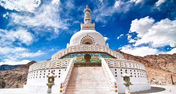 Strahlend weiße Stupa mit Kuppel und kunstvollen Wandmalereien, die sich gegen einen dramatischen Himmel erhebt.
