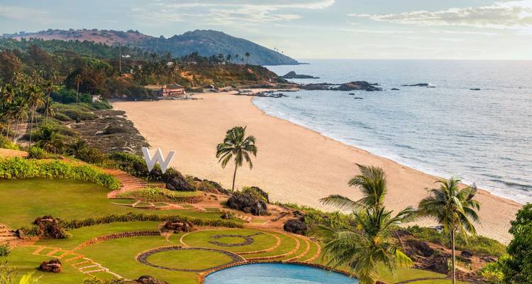 Vista aérea de un resort costero de lujo con jardines bordeados de palmeras y una amplia bahía de arena.