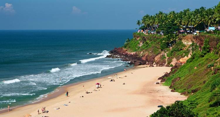 Breiter goldener Sandstrand mit sanften Wellen und üppig grüner Klippe in Varkala