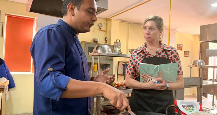 El chef instruye a un turista que toma notas durante una clase de cocina práctica en una cocina.