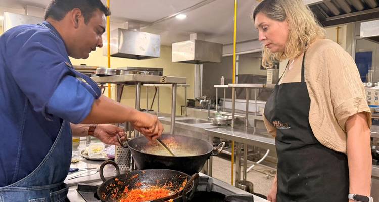 El instructor revuelve un wok de comida mientras el participante observa durante un taller culinario.