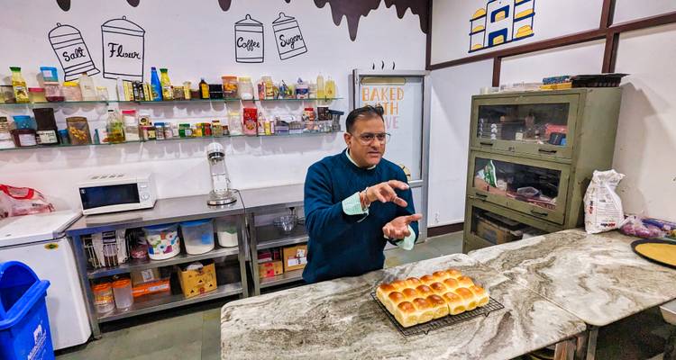 El instructor muestra con orgullo una bandeja de pan recién horneado dentro de una cocina de enseñanza.