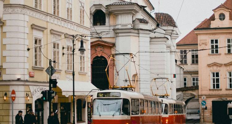 Eine klassische rot-cremefarbene Straßenbahn fährt an historischen pastellfarbenen Gebäuden auf einer Kopfsteinpflasterstraße in Prag vorbei.
