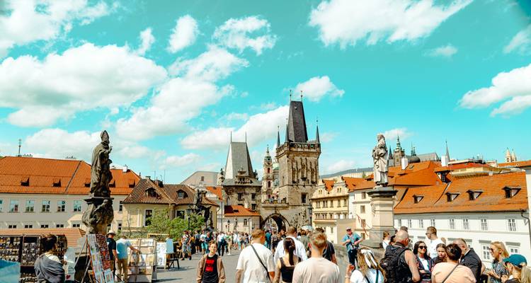 Sonniger Tag mit Menschenmenge, die die mit Statuen gesäumte Karlsbrücke überquert, und Stadttürme unter einem leuchtend türkisfarbenen Himmel.