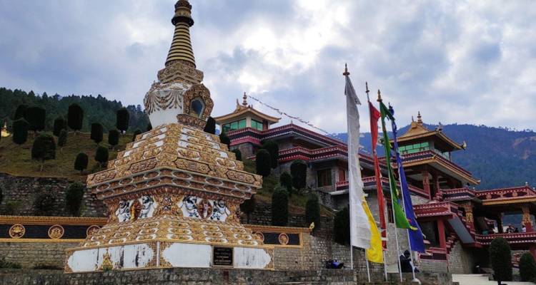 Goldene Stupa und Klosterkomplex eingerahmt von Bergen und dramatischem bewölktem Himmel.