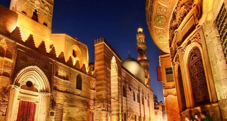 Sfeervolle nachtscène van sierlijke islamitische architectuur verlicht met gouden lampen langs een smal straatje.