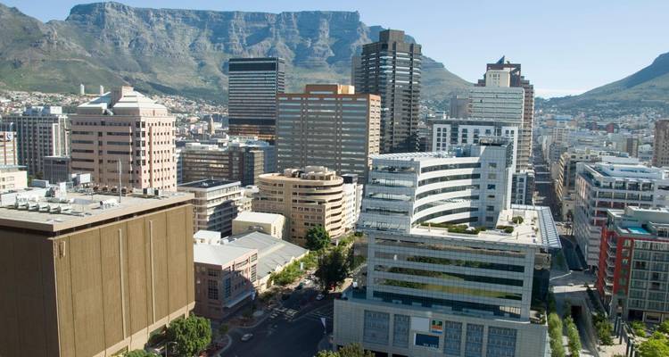 Modernes Hochhaus-Stadtzentrum Kapstadts mit dramatischer Tafelberg-Kulisse unter klarem Himmel.