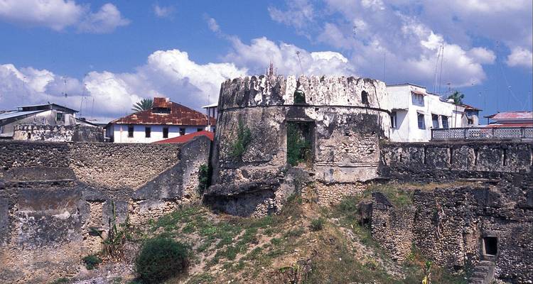 Muros de piedra rugosos y baluartes de un fuerte antiguo contrastados contra el cielo azul y los tejados esparcidos del pueblo.