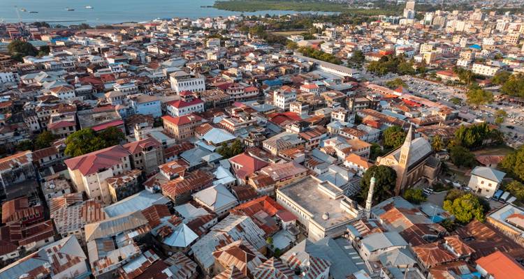 Vista panorámica aérea de los densos tejados de Stone Town con el mar turquesa y la costa a lo lejos.