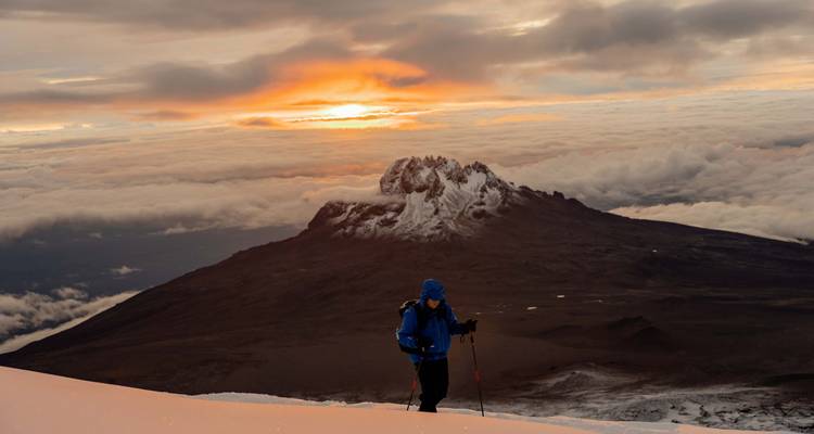 Un alpiniste en solo ascension gravit une pente enneigée avec le lever de soleil flamboyant derrière le pic rocheux de Mawenzi.