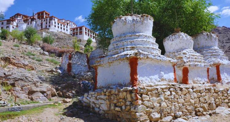Weiß getünchte Chorten und ein Gipfelkloster vor einem strahlend blauen Himmel und felsigem Gelände in Ladakh.