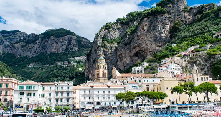 Charmante ville d'Amalfi avec des bâtiments côtiers aux couleurs pastel et un clocher d'église situés sous des falaises abruptes et des terrasses verdoyantes.