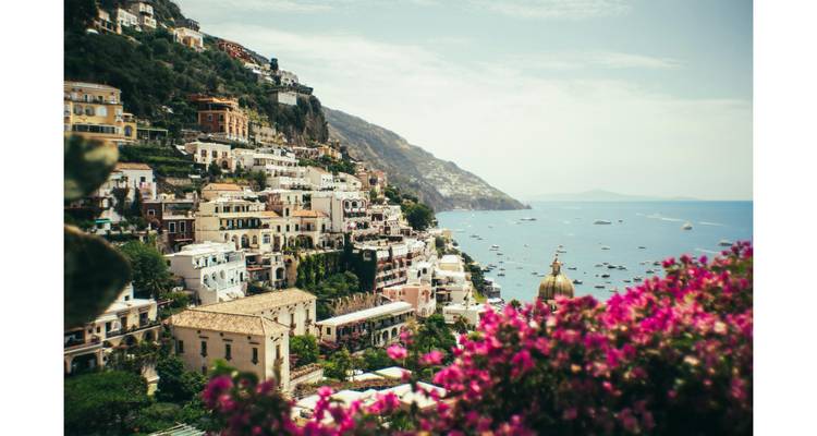 Les maisons colorées accrochées à la falaise s'étagent vers la mer turquoise le long de la Côte d'Amalfi en Italie, avec un éclatant bougainvillier au premier plan.