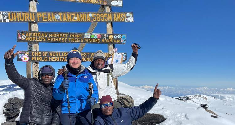 Les grimpeurs célèbrent à la pancarte du Uhuru Peak lors d'une journée de sommet ensoleillée.