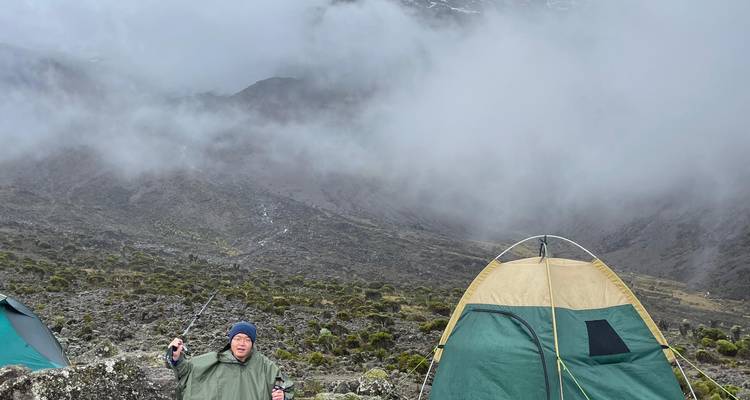 Un campeur en poncho se tient à côté d'une tente au milieu d'une brume de montagne tourbillonnante.