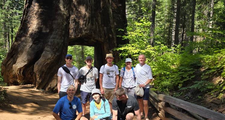 Grupo de senderistas posa debajo del túnel tallado a través de un árbol secuoya caído masivo en Yosemite.