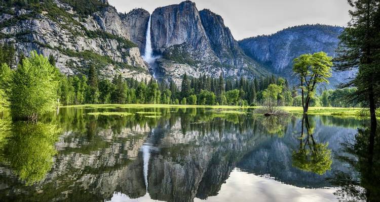 Prado inundado como un espejo refleja las cataratas de Yosemite y acantilados de granito bajo luz suave.